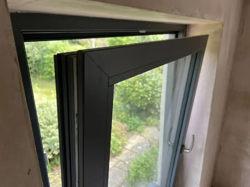 Hoek van een antracietgrijs aluminium draaikiepraam met smal profiel en driedubbel glas, van binnenuit gezien